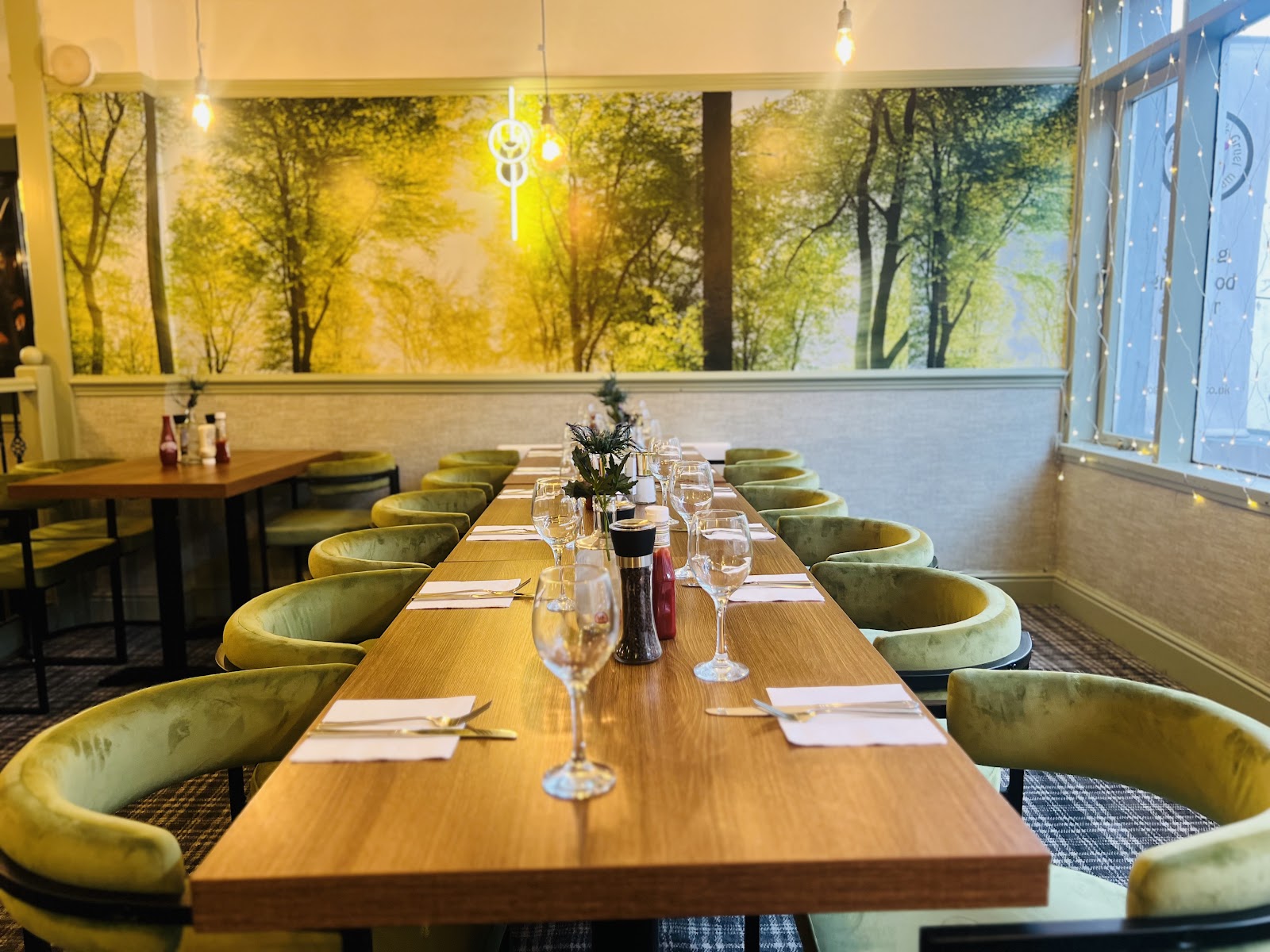 The Malt Man dining room — long oak table set for a party, sage-green velvet chairs and warm pendant lighting (photo: The Malt Man)